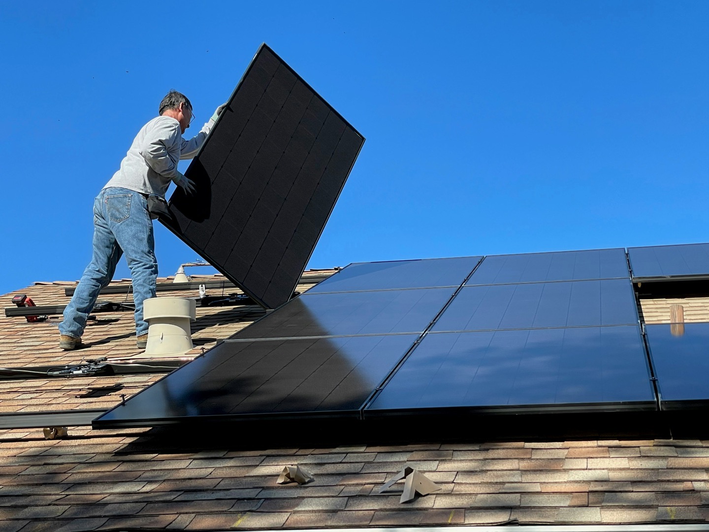 Technician installing a black solar panel on a residential roof in the Dubuque, Iowa area